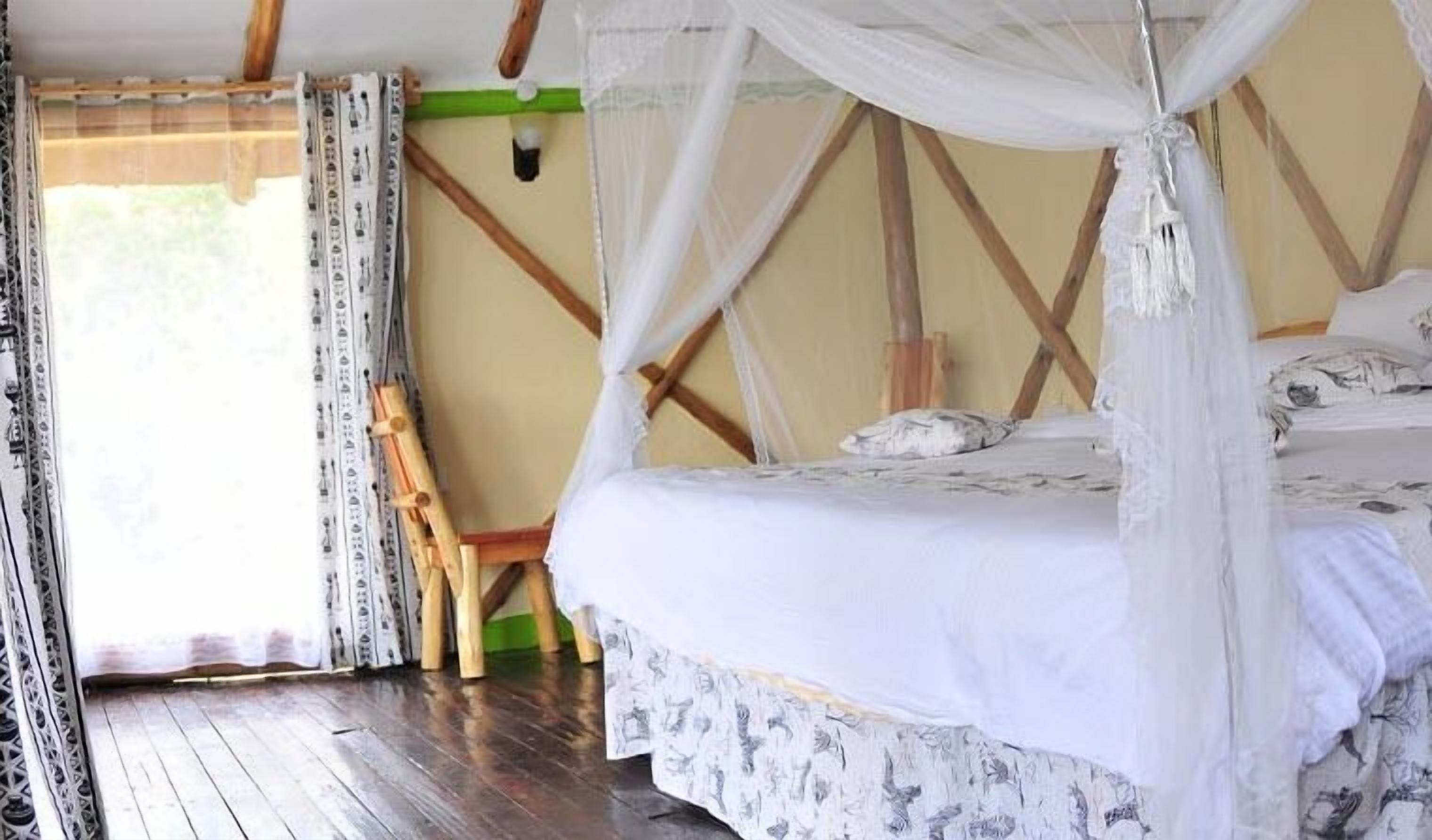 Una habitación con cama bajo un dosel, una silla de madera y un ventanal con cortinas.