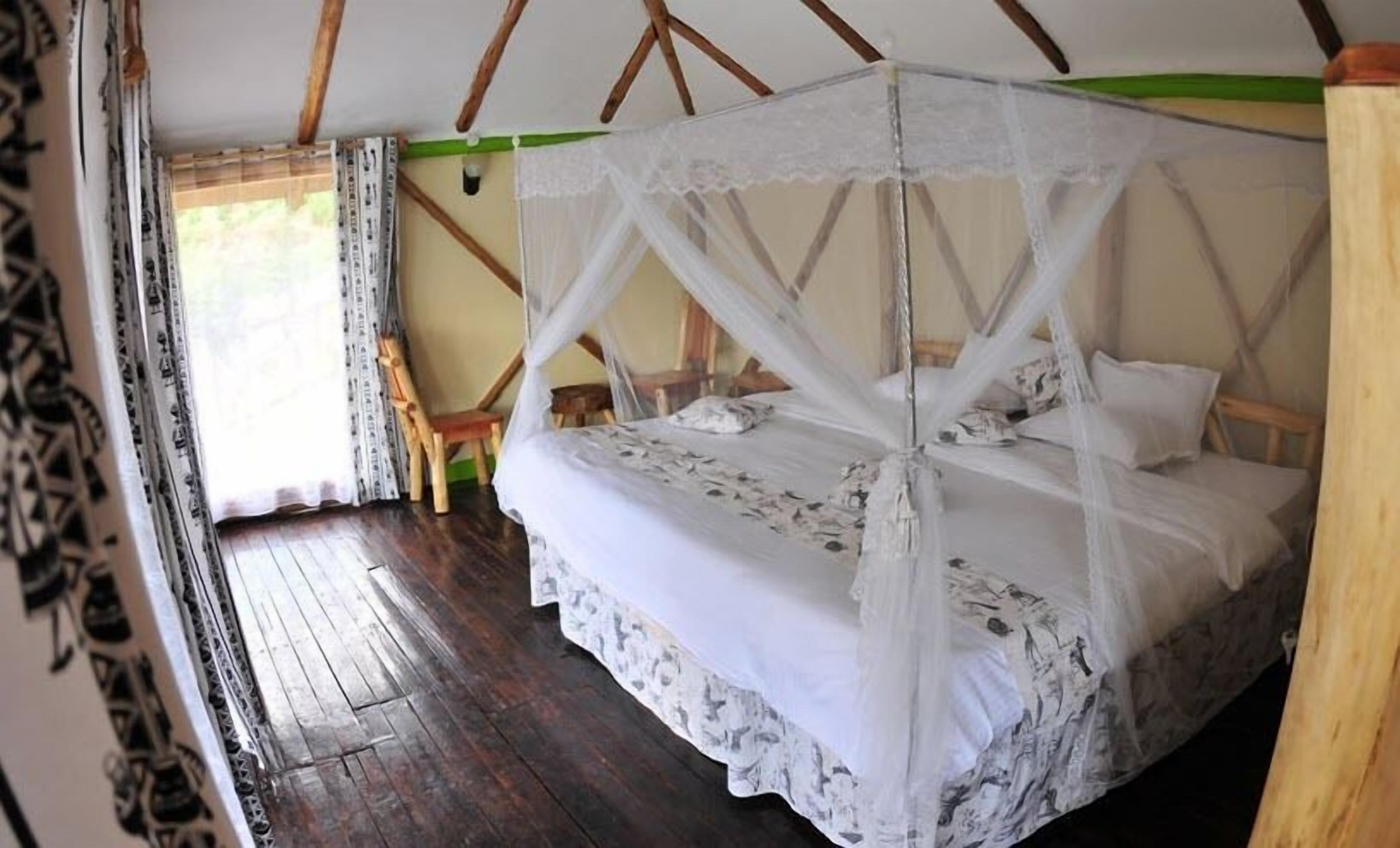 A single bed with a canopy, wooden flooring, and a chair in a room with a sloped ceiling.