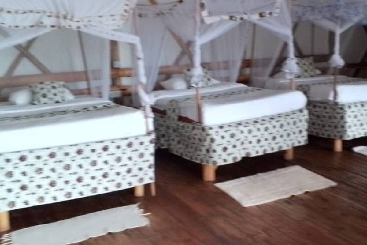 Een kamer met drie bedden, elk voorzien van een hemelbed. De bedden hebben beddengoed met een patroon. Op de vloer staat een houten stoel en een klein tapijt.