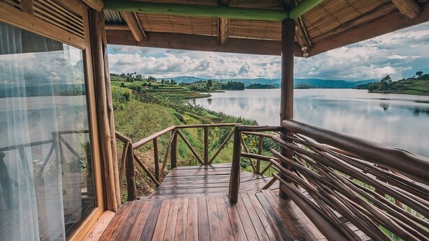 Una terraza de madera con barandilla, con vista a un lago tranquilo y colinas verdes.