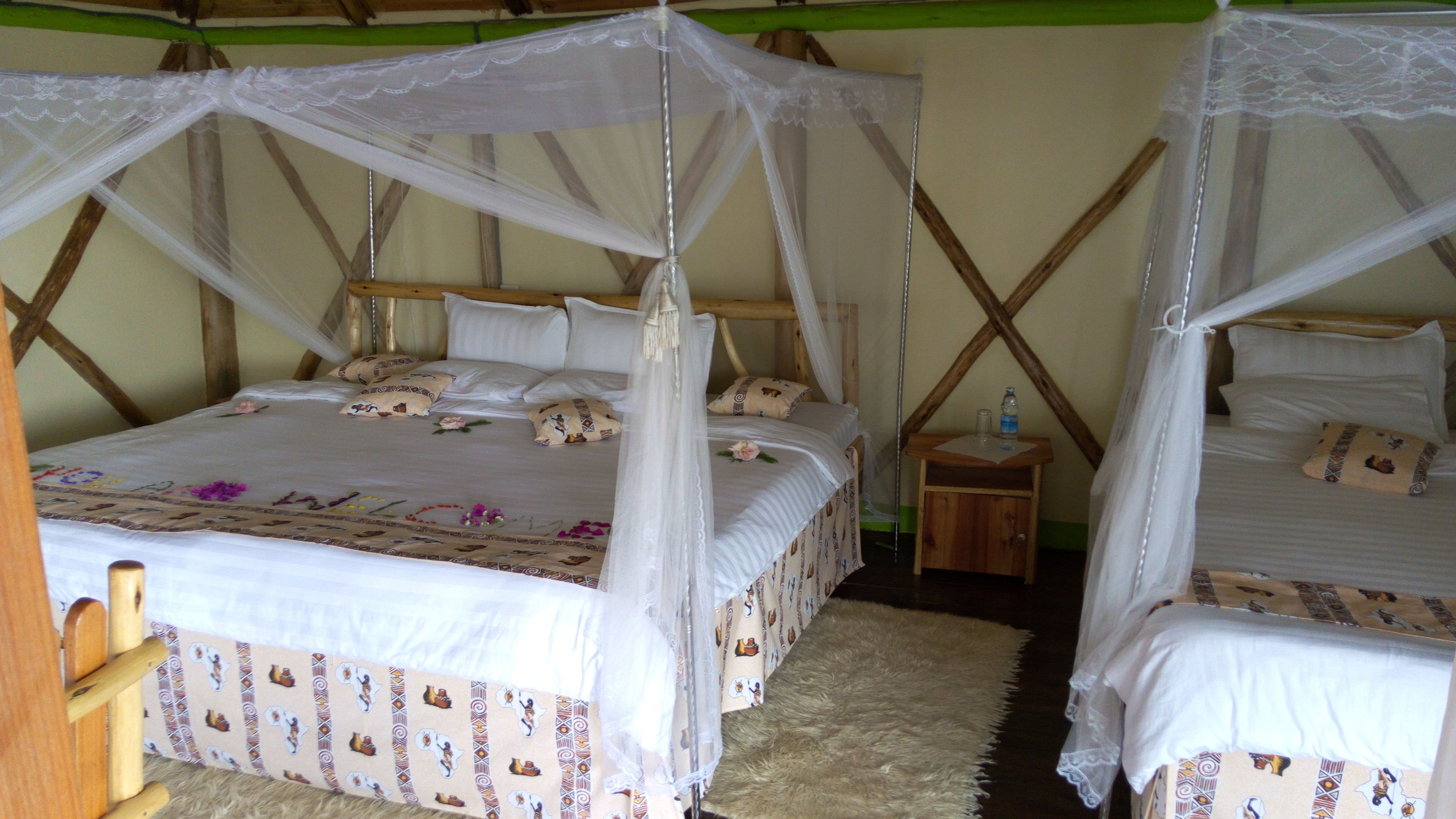 A room with two beds, each with a canopy bedspread and pillows. There is a small wooden nightstand with a water bottle on it.
