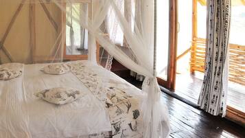 A bed with a canopy, pillows, and a patterned bedspread in a room with wooden floors and a window.