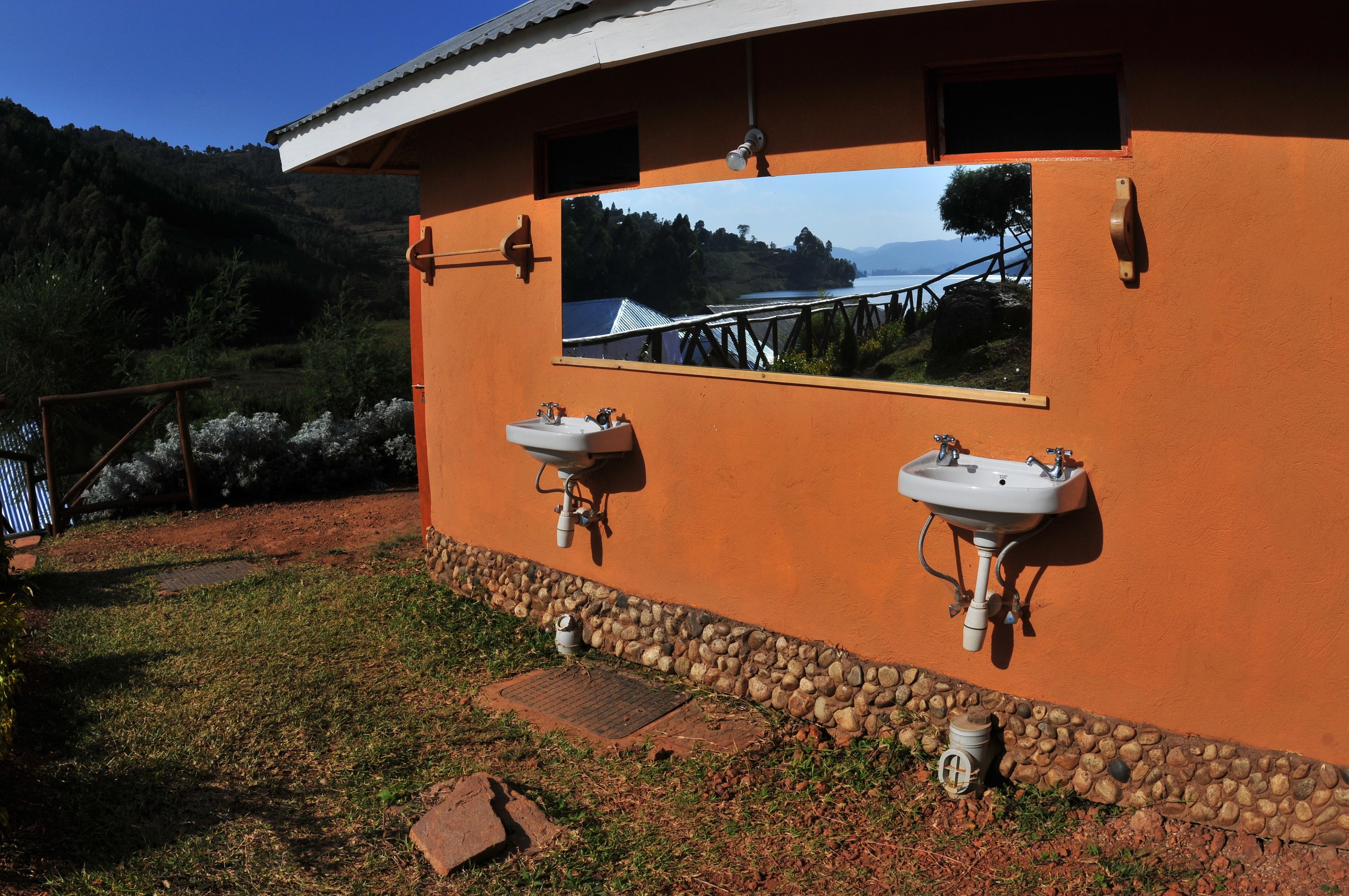 A building with two sinks mounted on an orange wall, a window with a scenic view, and a stone border.