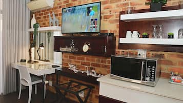 Un espacio habitable compacto con un televisor montado en una pared de ladrillo, una mesa de comedor con sillas, un microondas y estantes con objetos decorativos.