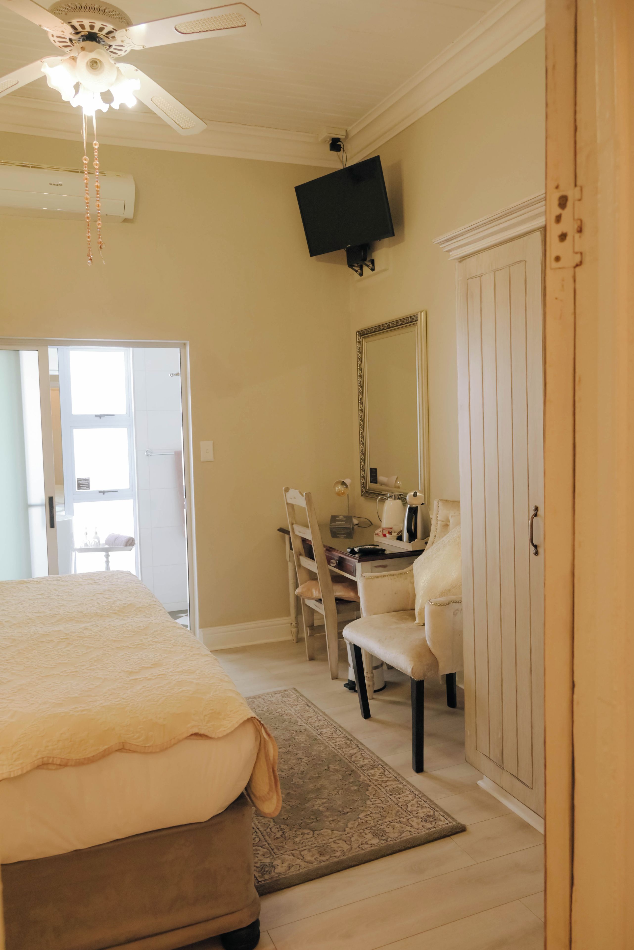 A bedroom with a bed, a desk, a chair, a wardrobe, a television, and a ceiling fan.