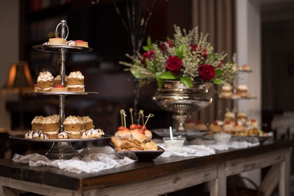 Um buffet de sobremesas com vários níveis de bolos e doces, um vaso com rosas vermelhas e um castiçal.