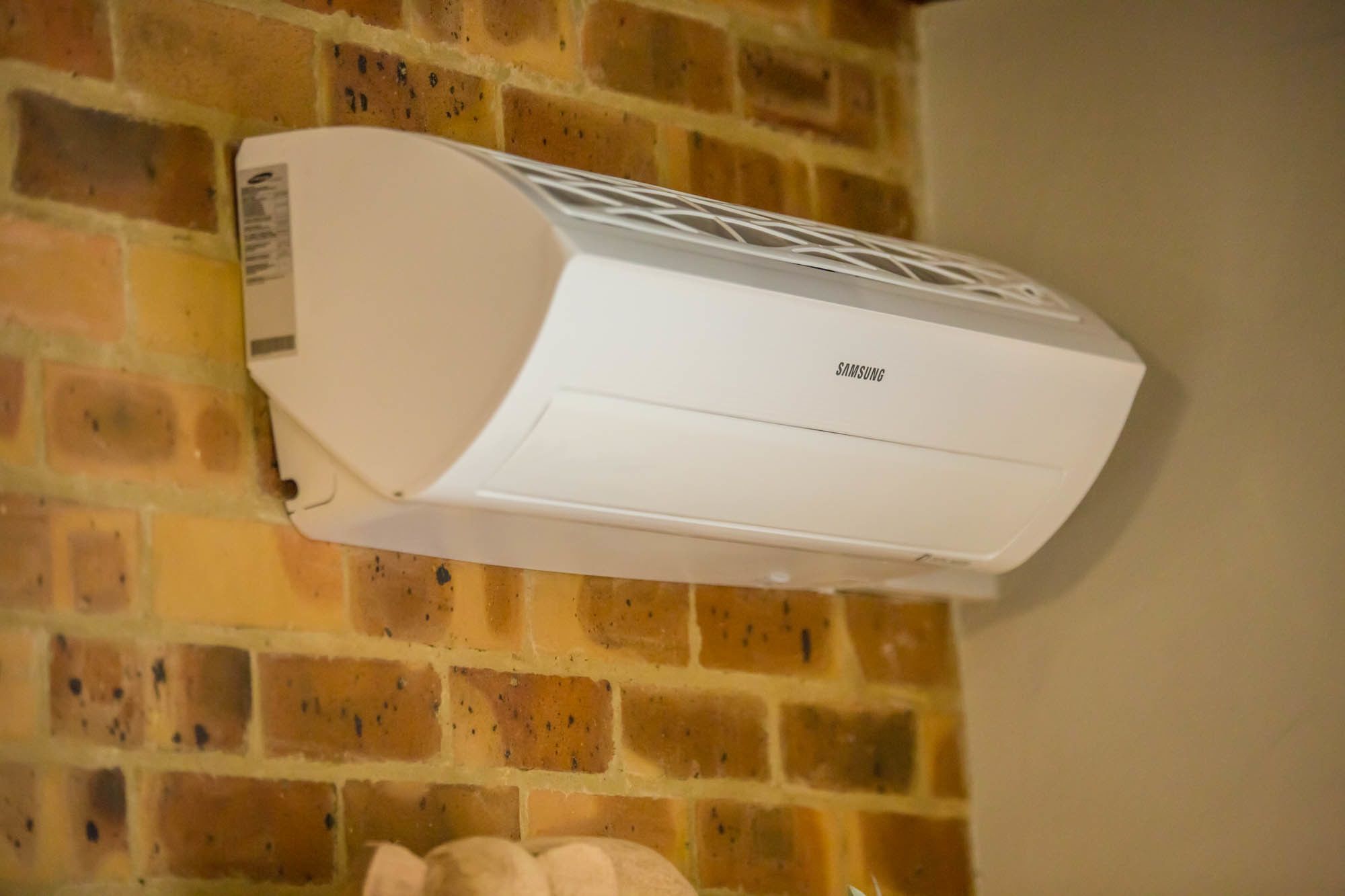 A white Samsung air conditioner mounted on a brick wall.
