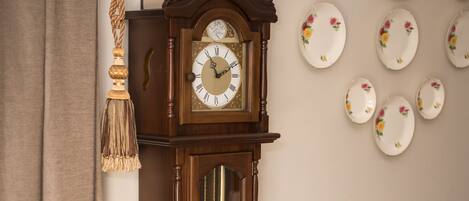 Une horloge comtoise traditionnelle en bois, dotée d’une porte en verre, est placée à côté d’une table à manger et de ses chaises.