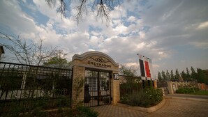 The entrance to Grey Manor Guesthouse, featuring a gated entrance, a number 76 sign, and a clear sky with clouds. - Grey Manor Guesthouse (Potchefstroom)