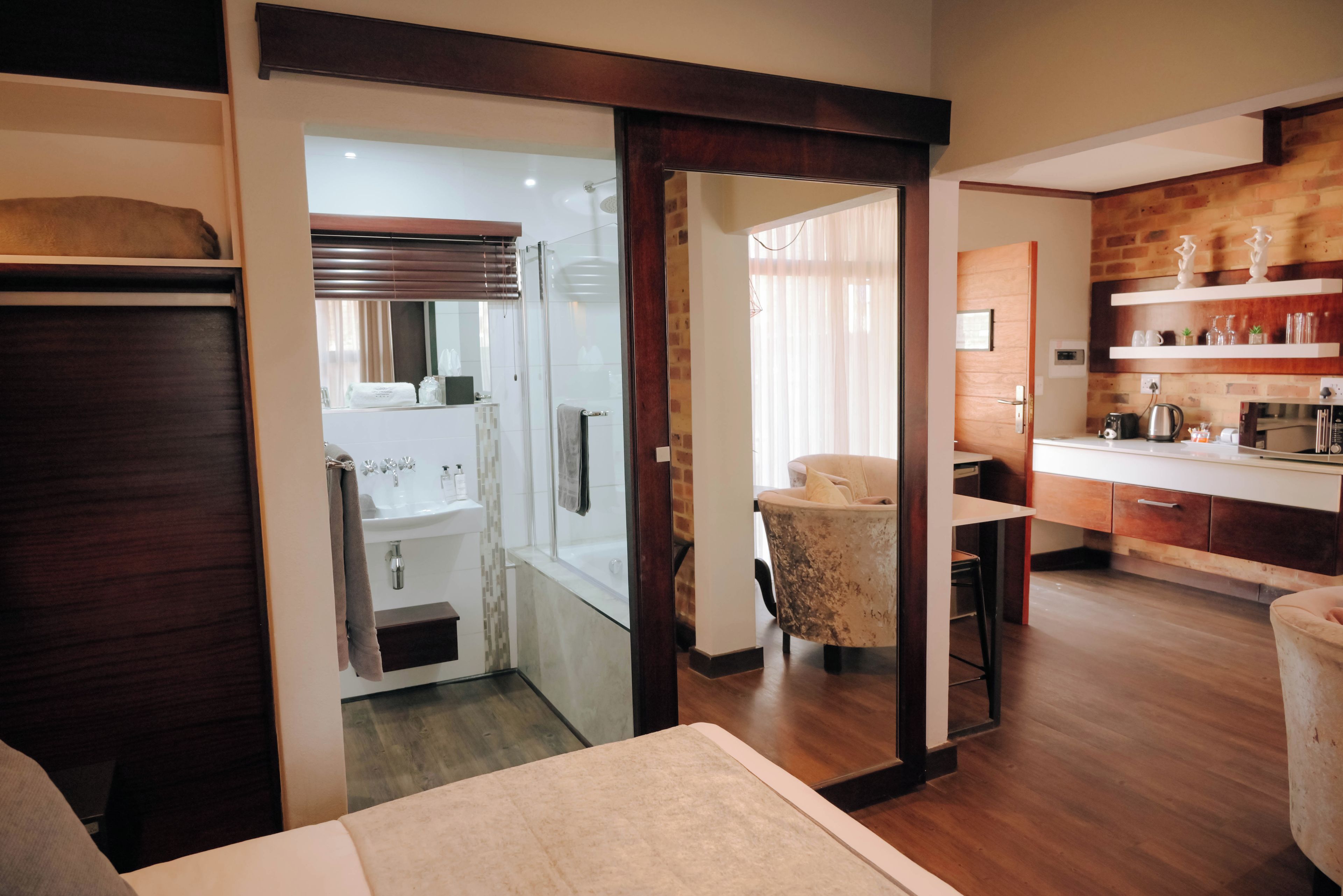 A modern interior with a wooden floor, a glass shower enclosure, a white sink, and a kitchen area with a wooden countertop and shelves.
