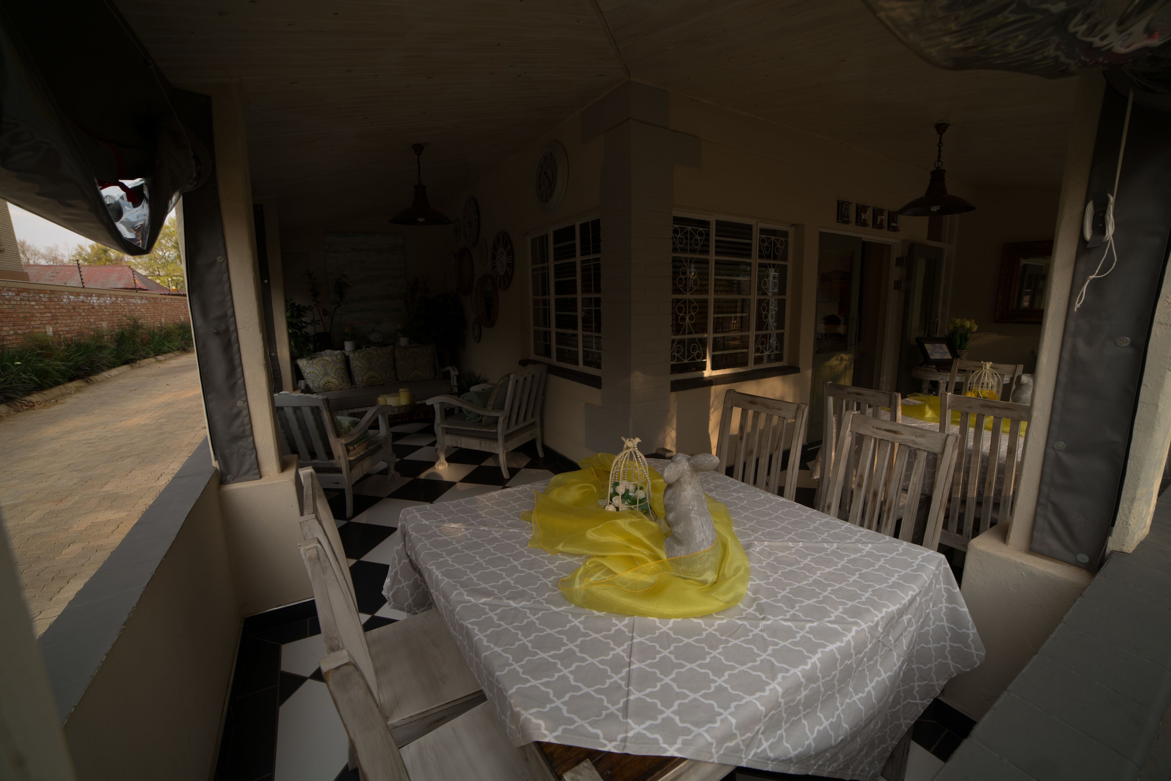 Un área de comedor al aire libre techada con una mesa preparada para dos, rodeada de sillas de madera.