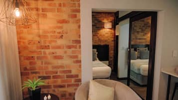 Une pièce avec un mur en briques, un lit avec une tête de lit, une chaise avec un coussin, une petite table avec une plante et un luminaire suspendu.