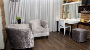 A modern room with a grey armchair, a white desk, and a small ottoman. There is a potted plant and a hanging light fixture. - Grey Manor Guesthouse (Potchefstroom)