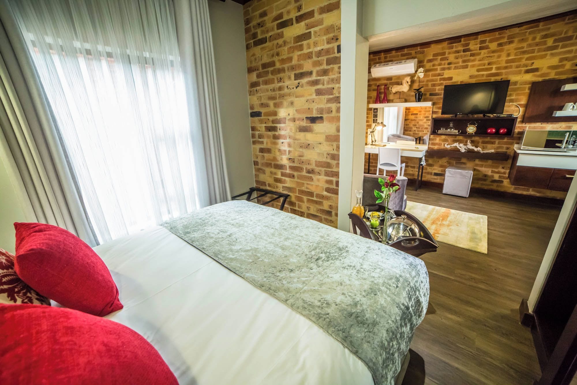 A hotel room with a bed, a dining area with a brick wall, and a television.