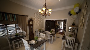 A dining area with a chandelier, white chairs, and a table set for four. - Grey Manor Guesthouse (Potchefstroom)
