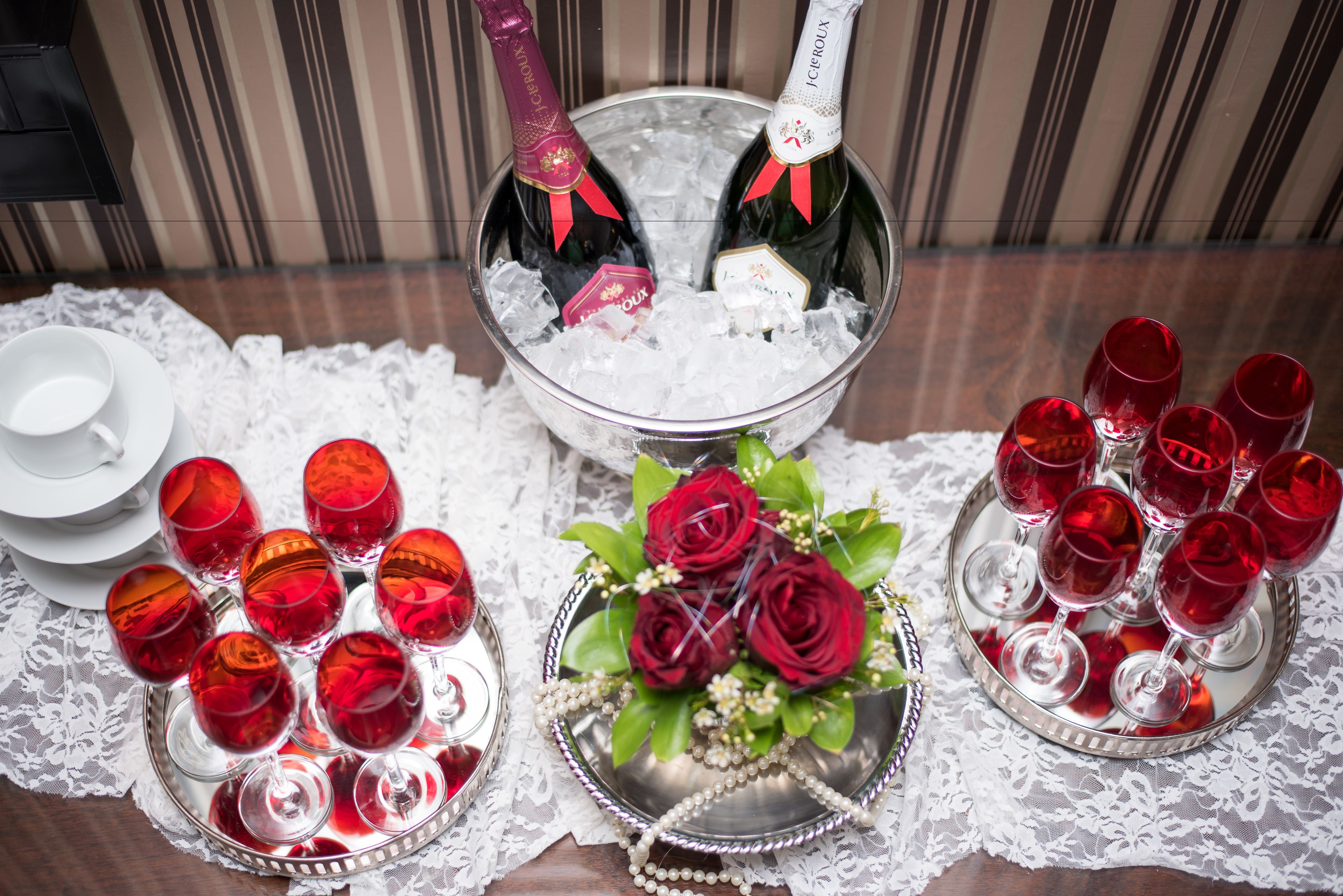 A table with a decorative arrangement including a bottle of champagne, red wine glasses, and a bouquet of roses.