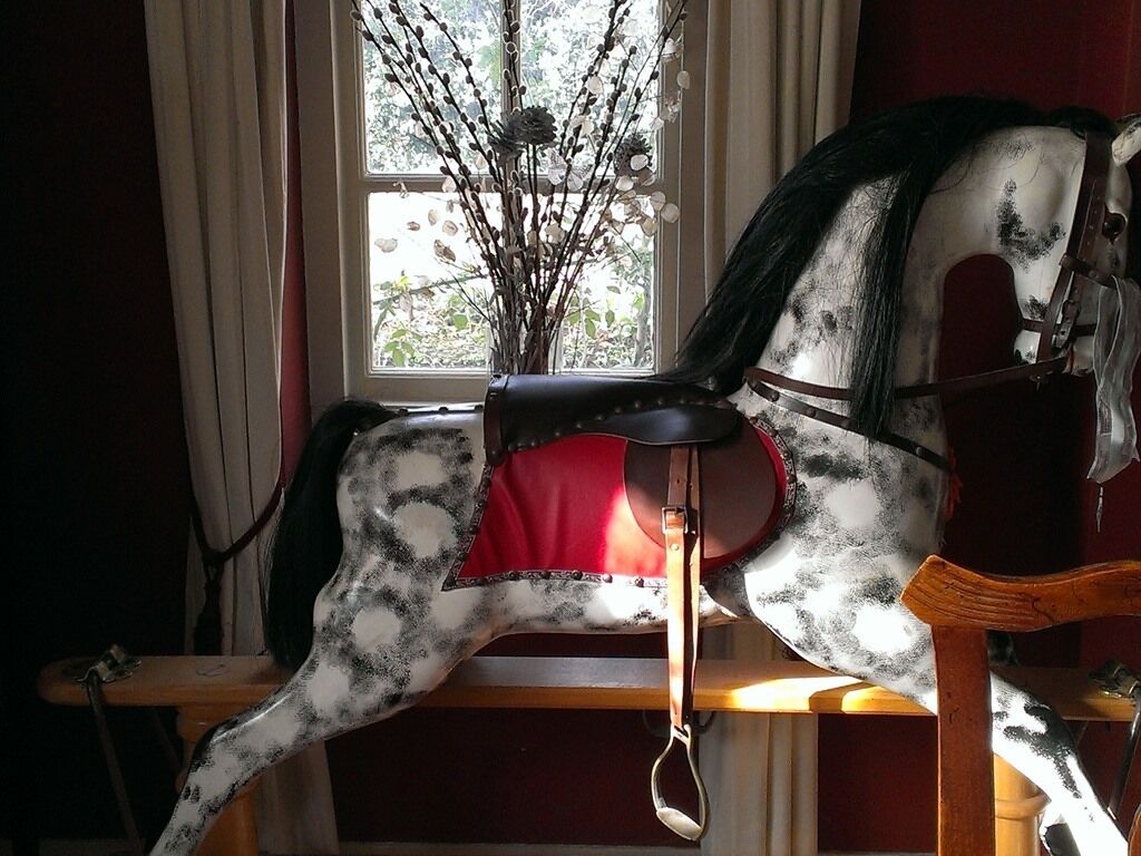 Ein Schaukelpferd in einem Zimmer mit Fenster und einer Vase mit Zweigen.