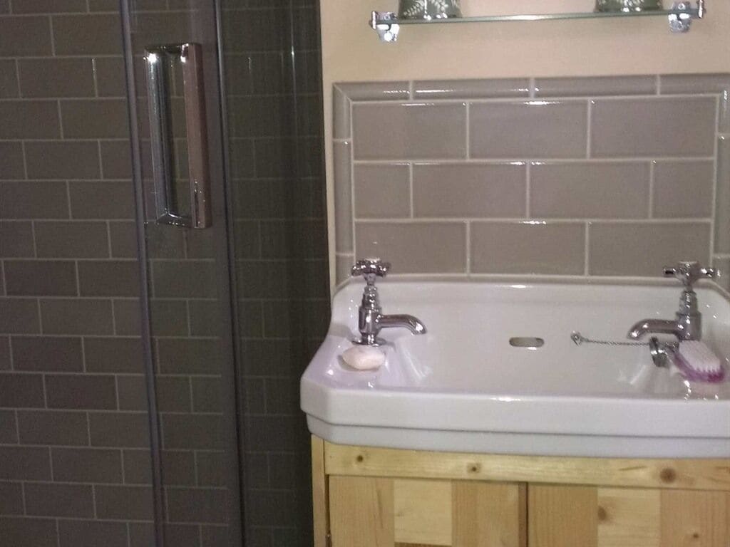 A bathroom with a white sink, two faucets, and a soap dish. There is a wooden cabinet below the sink.