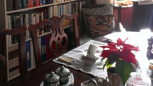 Un coin lecture confortable avec un fauteuil en bois, une bibliothèque remplie de livres, une table avec une théière et une plante en pot.