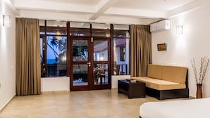 A hotel room with a sofa, a bed, a small table, and a view of the outside. - Green Parrot Beach Resort (Rekawa)