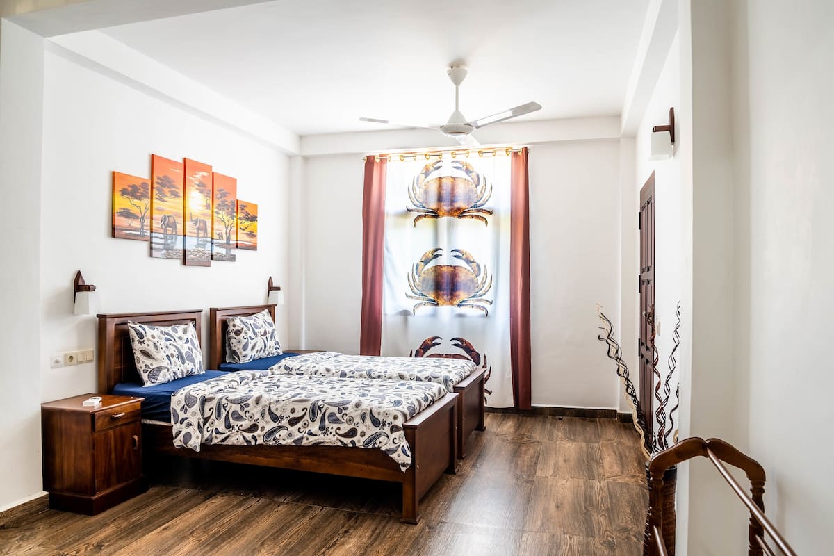 A bedroom with a wooden bed, a nightstand, a ceiling fan, and a window with curtains.