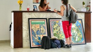 A reception desk with a framed map, a vase of yellow flowers, and a painting of a sailboat. - Green Parrot Beach Resort (Rekawa)