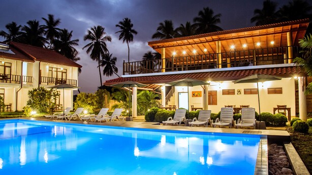 A swimming pool with lounge chairs, a covered patio, and a building with a balcony. - Green Parrot Beach Resort (Rekawa)
