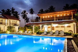 A swimming pool with lounge chairs, a covered patio, and a building with a balcony. - Green Parrot Beach Resort (Rekawa)
