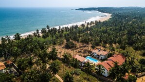 A coastal property with a swimming pool, surrounded by palm trees and a beach. - Green Parrot Beach Resort (Rekawa)