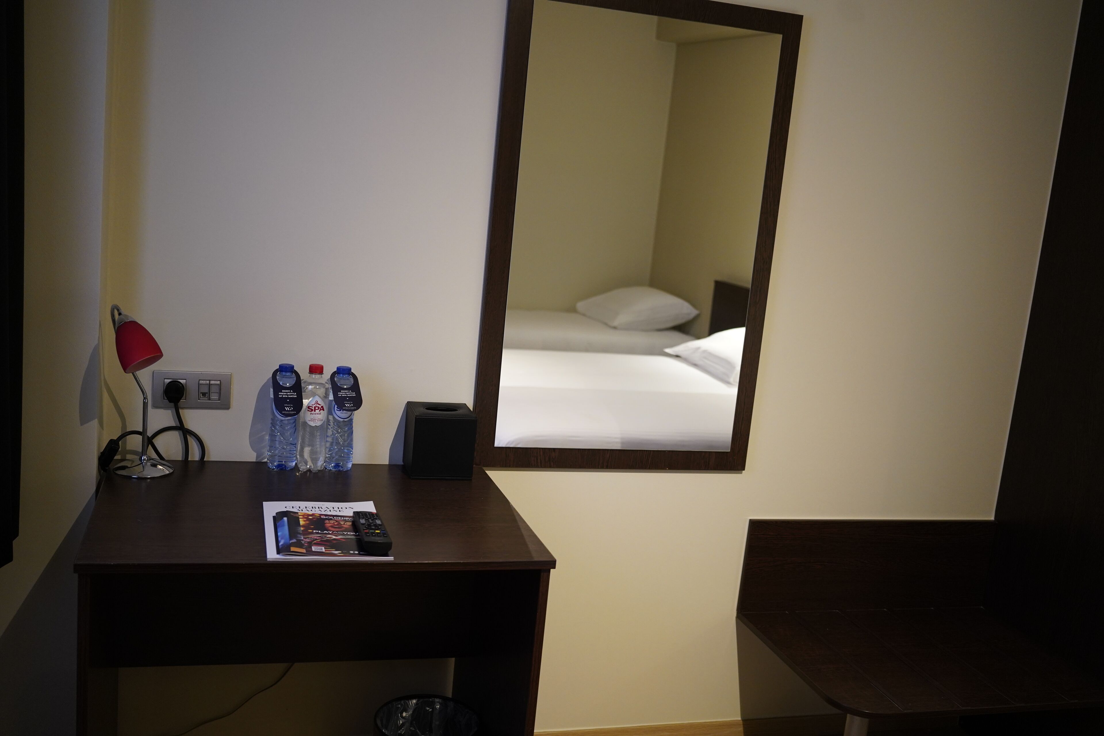 Une chambre d’hôtel avec un lit, un bureau doté d’une lampe et un miroir qui reflète le lit.