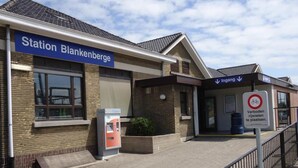 Una estación de tren llamada 'Station Blankenberge' con una máquina de venta de billetes y un cartel que indica 'Ingang' (entrada).