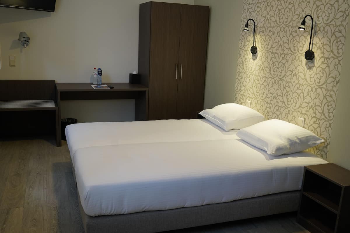 A hotel room with a bed, a desk, a wardrobe, and two wall-mounted lights.
