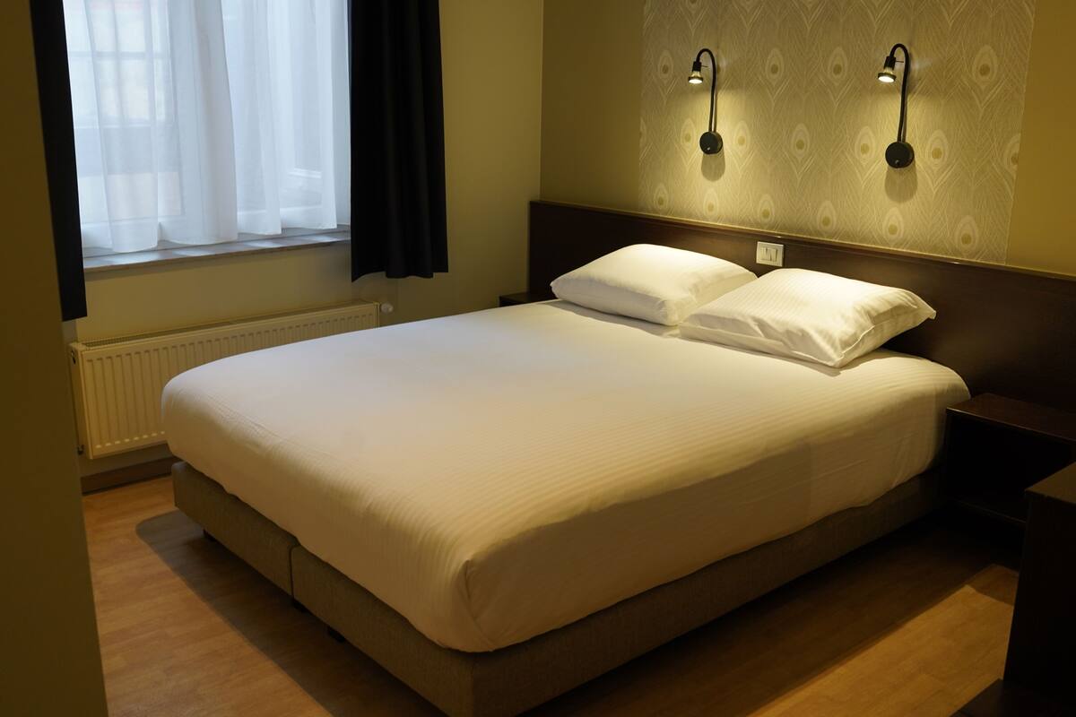 A neatly made bed with white linens in a hotel room.