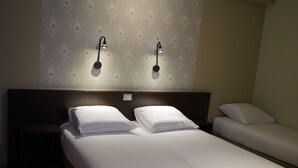 Habitación de hotel con dos camas individuales, cabecera de madera y lámparas de lectura fijadas a la pared.