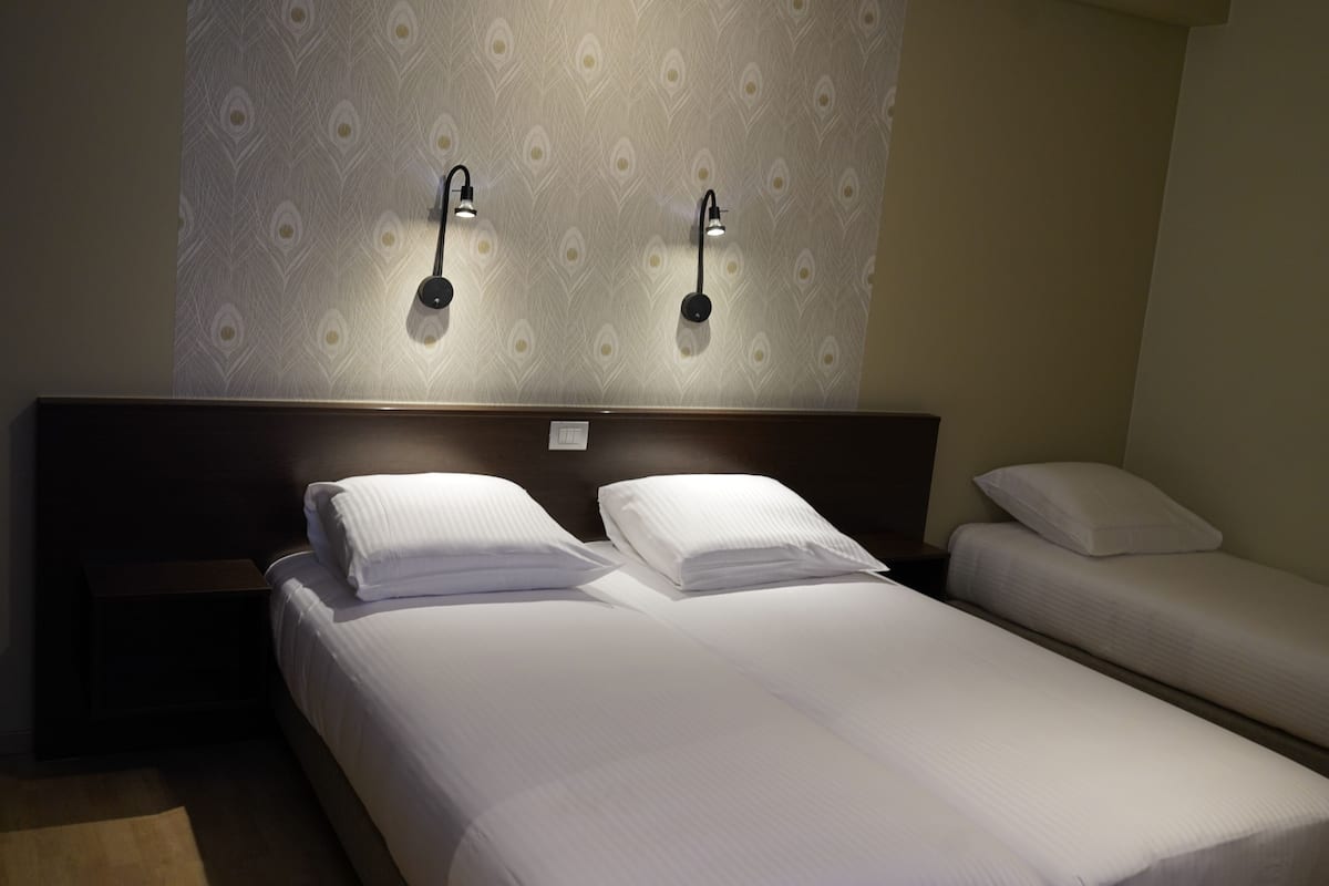 A hotel room with two single beds, a wooden headboard, and wall-mounted reading lights.