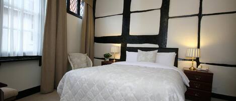 A bedroom with a large bed, two bedside tables with lamps, a chair, and a window with curtains.