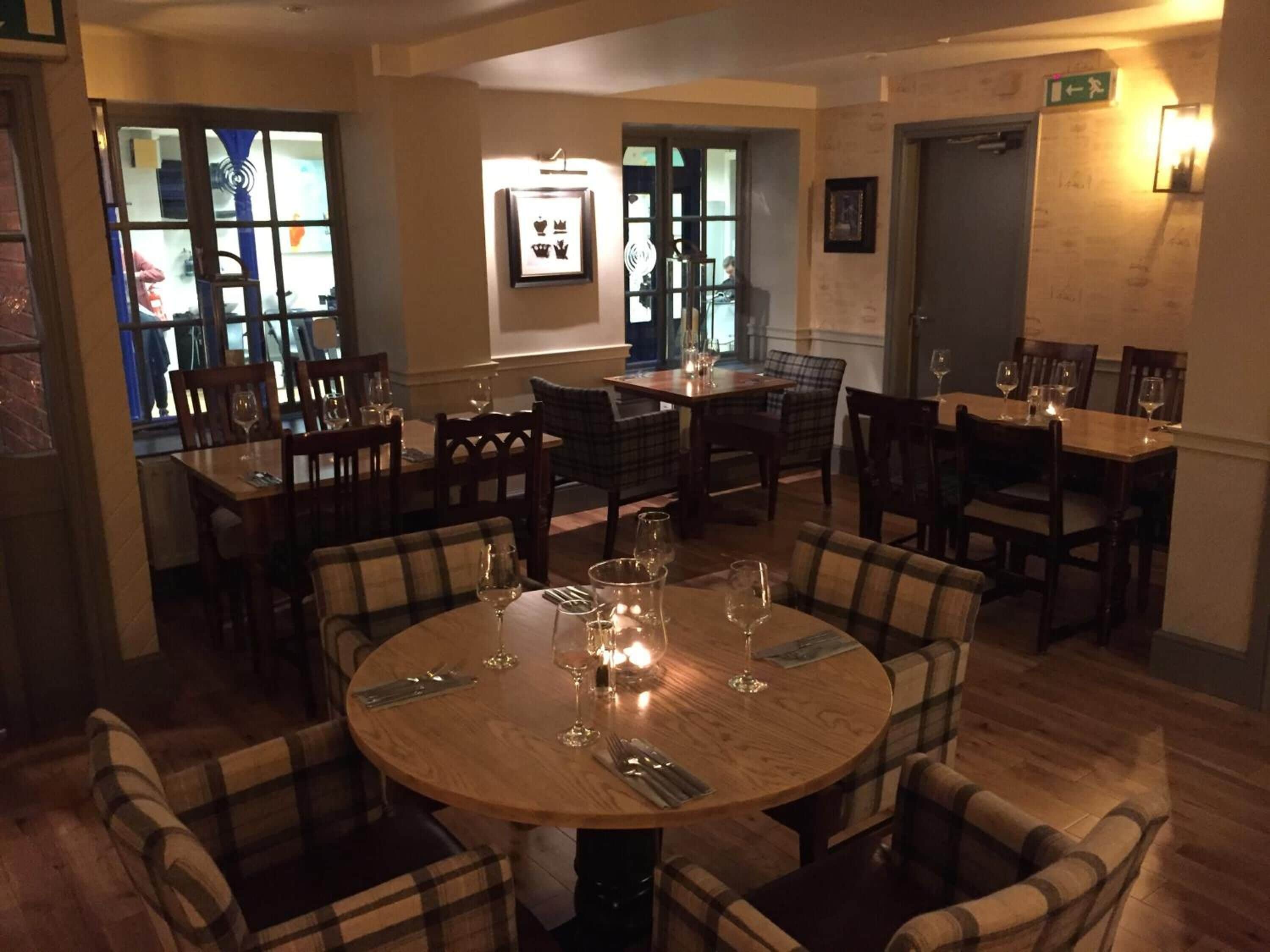 A restaurant interior with round tables, plaid chairs, and a warm ambiance.