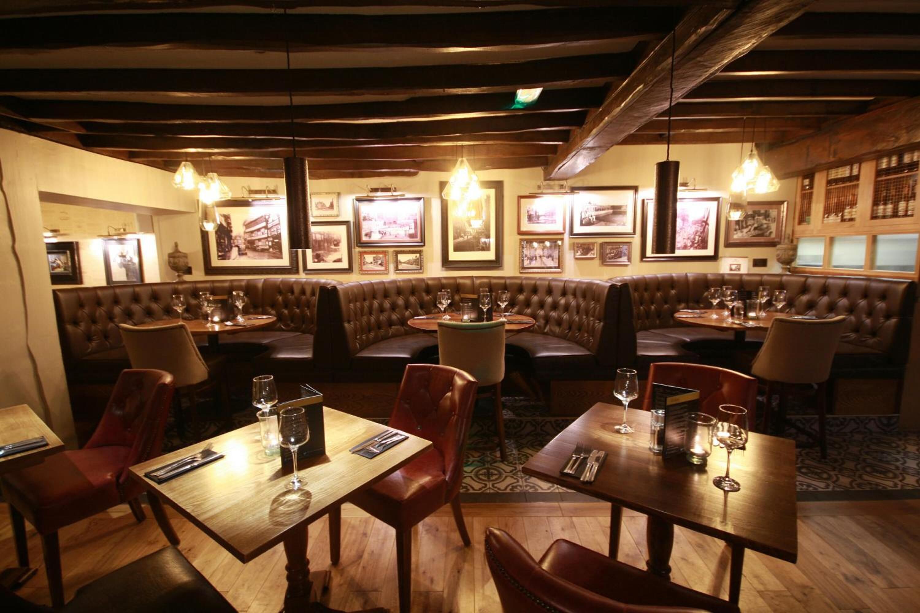Um restaurante com mesas e cabines de madeira, quadros nas paredes e luminárias pendentes.