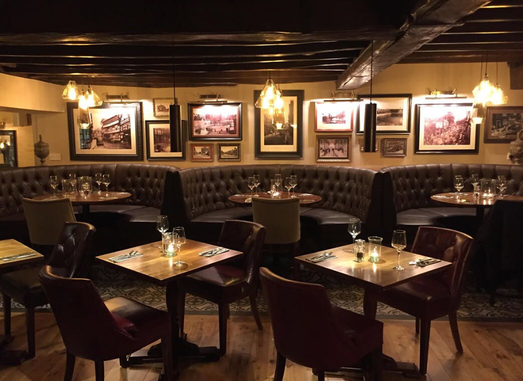 A restaurant with a cozy ambiance, featuring a mix of booths and tables, wooden flooring, and framed pictures on the walls.