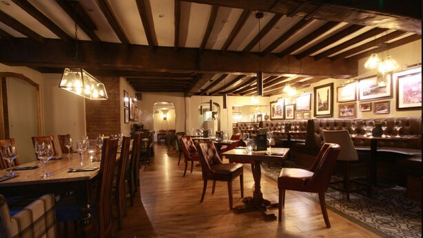 A restaurant with wooden tables and chairs, hanging lights, and framed pictures on the walls. - Crown Hotel (Nantwich)