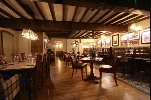 Un restaurante con mesas y sillas de madera, luces colgantes y cuadros en las paredes.