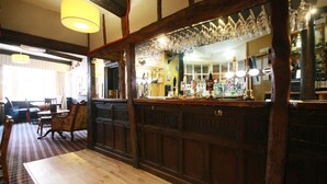 A bar area with wooden paneling, a counter with bottles and glasses, and a checkered floor. - Crown Hotel (Nantwich)