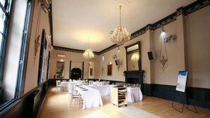 A spacious room with long tables set for dining, a chandelier, and a fireplace. - Crown Hotel (Nantwich)
