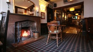 A cozy room with a fireplace, plaid carpet, wooden furniture, and a television in the background. - Crown Hotel (Nantwich)