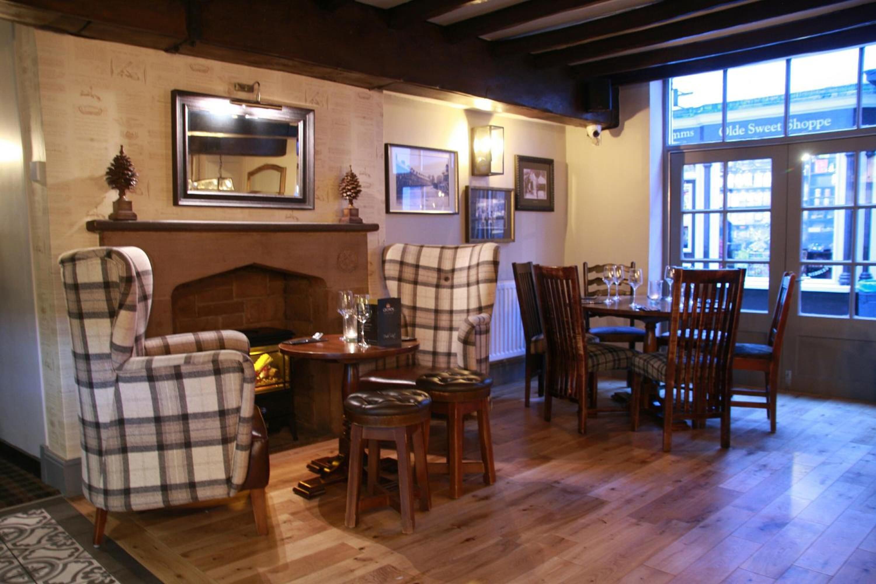 A cozy room with a fireplace, plaid chairs, a dining table with chairs, and a large window with a view of the street.