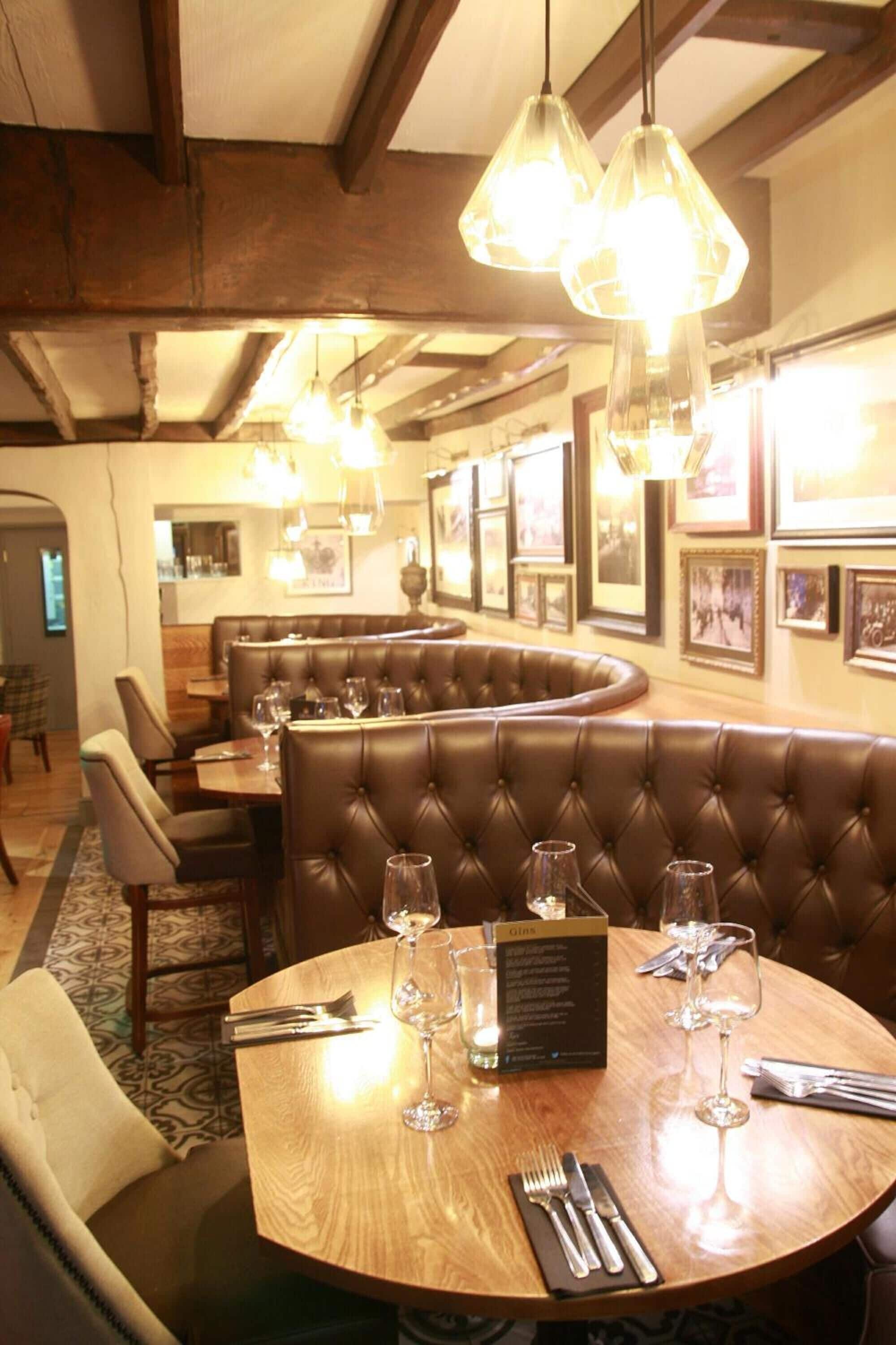 Un restaurante con una mesa de madera redonda dispuesta para dos personas, una zona de asientos tipo cabina e iluminación colgante.