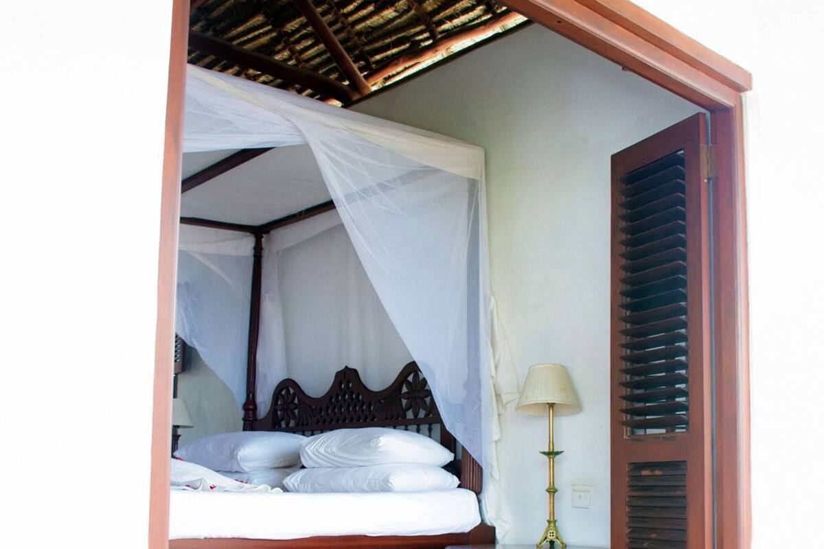 Ein Schlafzimmer mit einem Bett, einem Nachttisch, einer Lampe und einem Fenster mit Holzrahmen.