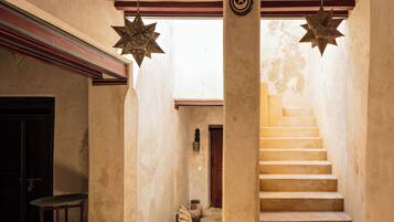 Un couloir étroit avec un banc en bois, un escalier orné d’un élément décoratif suspendu en forme d’étoile, et une série d’objets en céramique disposés le long du mur.