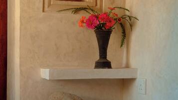 A bathroom with a beige wall, a white shelf with a vase of flowers, a towel rack, and a small mirror.