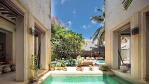 A pool area with a thatched-roof structure, surrounded by potted plants and lounge chairs.
